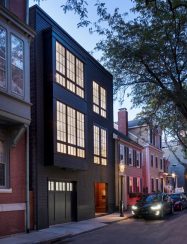 modern exterior of black 3-story row house glowing at dusk