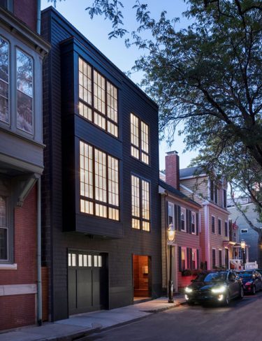 modern exterior of black 3-story row house glowing at dusk