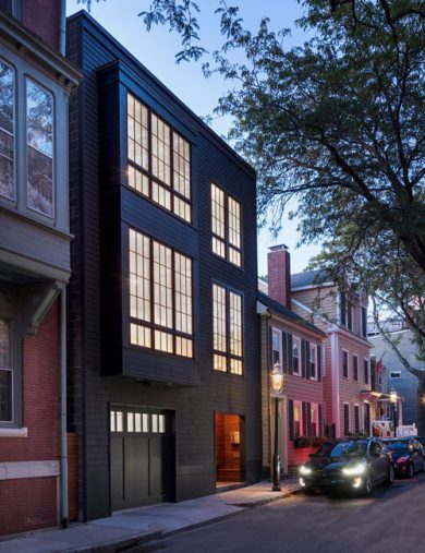 modern exterior of black 3-story row house glowing at dusk