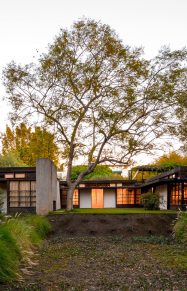 exterior of home at dusk with glowing windows surrounded by curated landscape