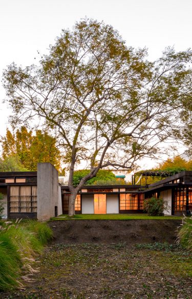 exterior of home at dusk with glowing windows surrounded by curated landscape