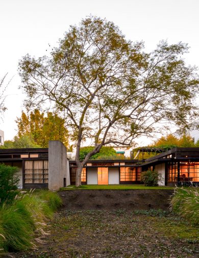 exterior of home at dusk with glowing windows surrounded by curated landscape