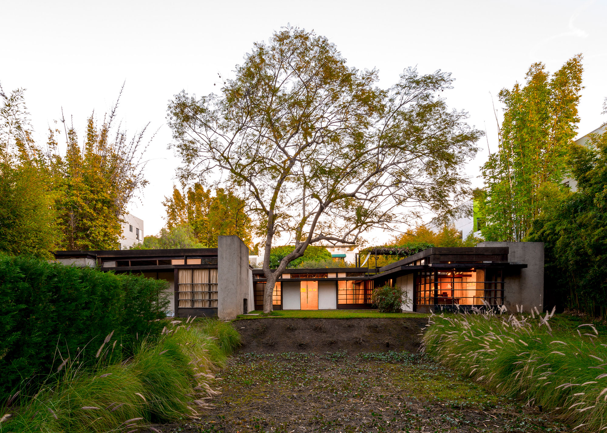 exterior of home at dusk with glowing windows surrounded by curated landscape