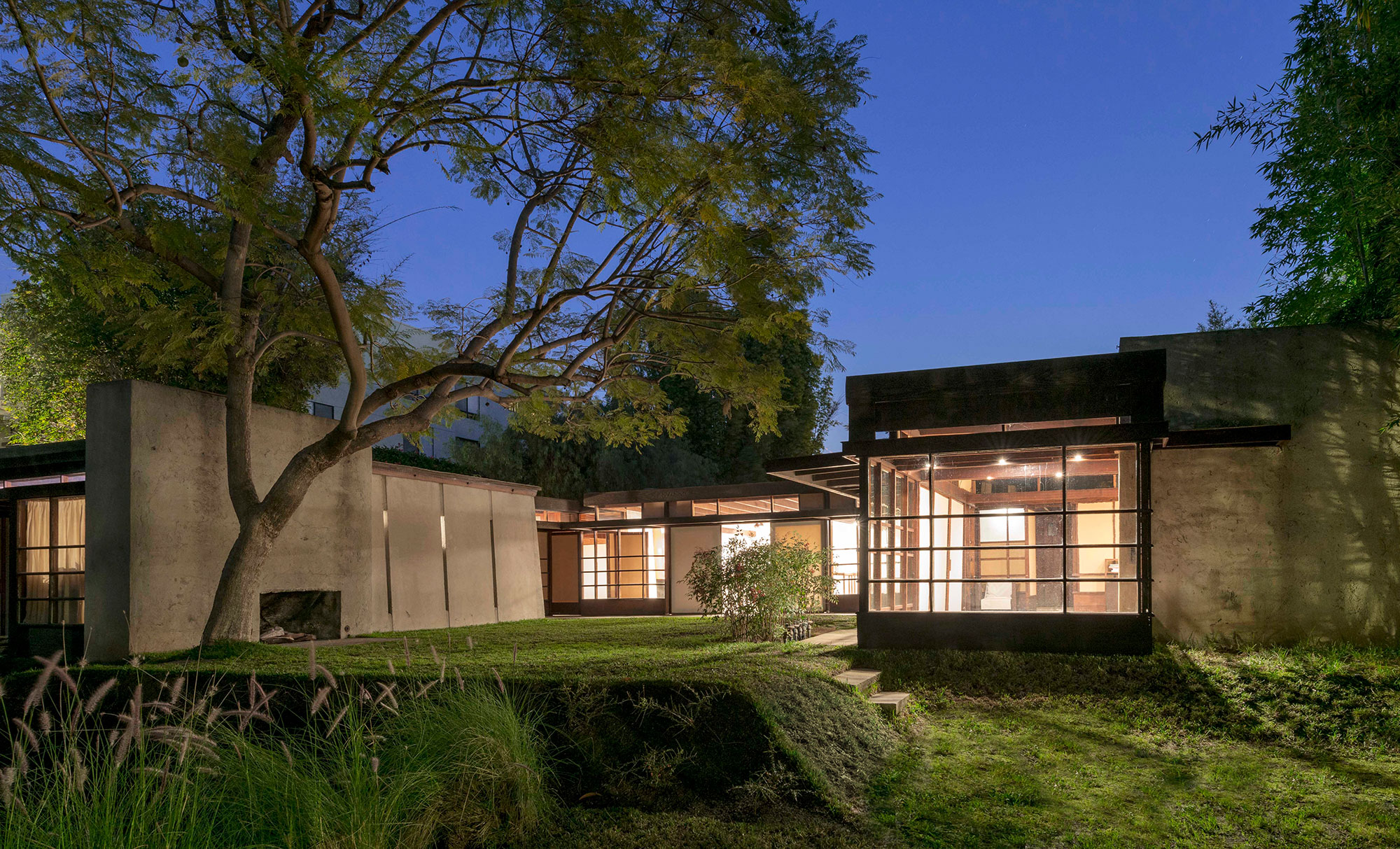 exterior of home at dusk with glowing windows surrounded by curated landscape