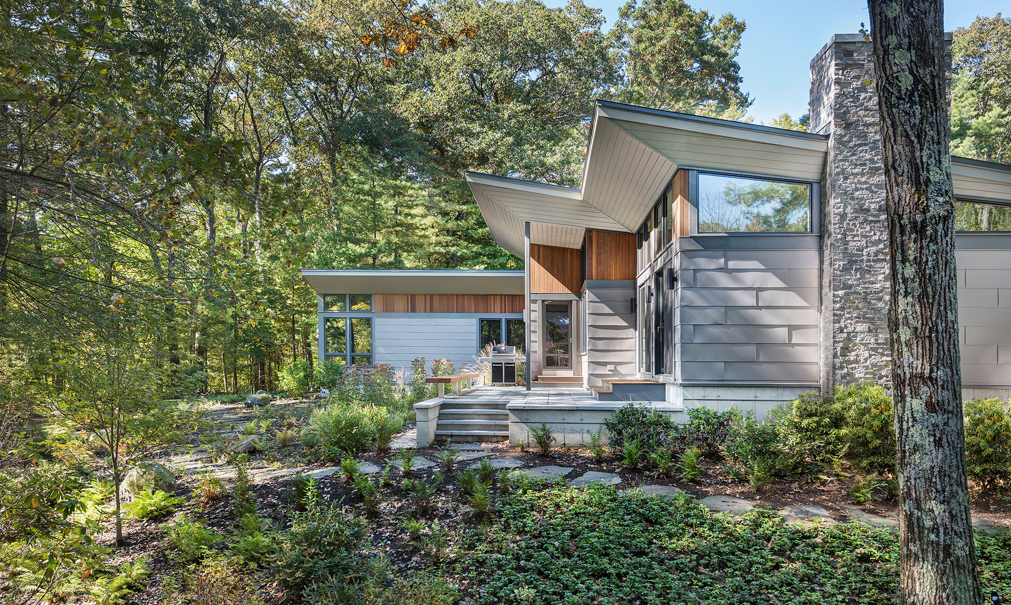 exterior of home with vertical cedar accents and warm grey metal siding and large stone chimney