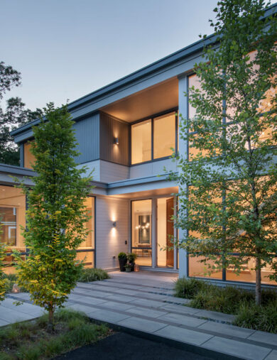 Evening lit front entrance with young trees and guiding walkway to home entrance.