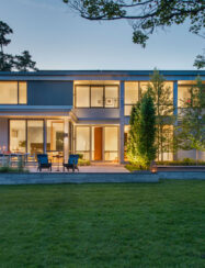 Evening front house view warmly lit by interior and outdoor lighting alongside exterior walls.