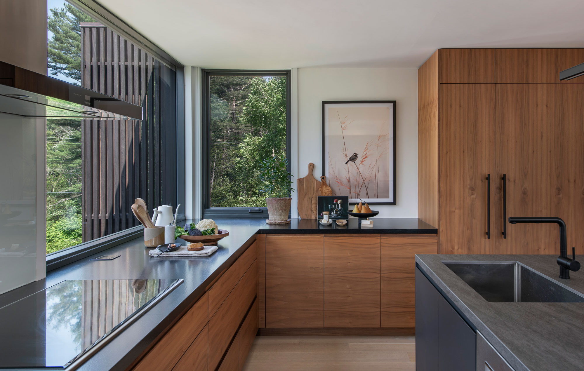 Open kitchen with wood cabinetry and black marble tabletops creating a minimal and sleek design.